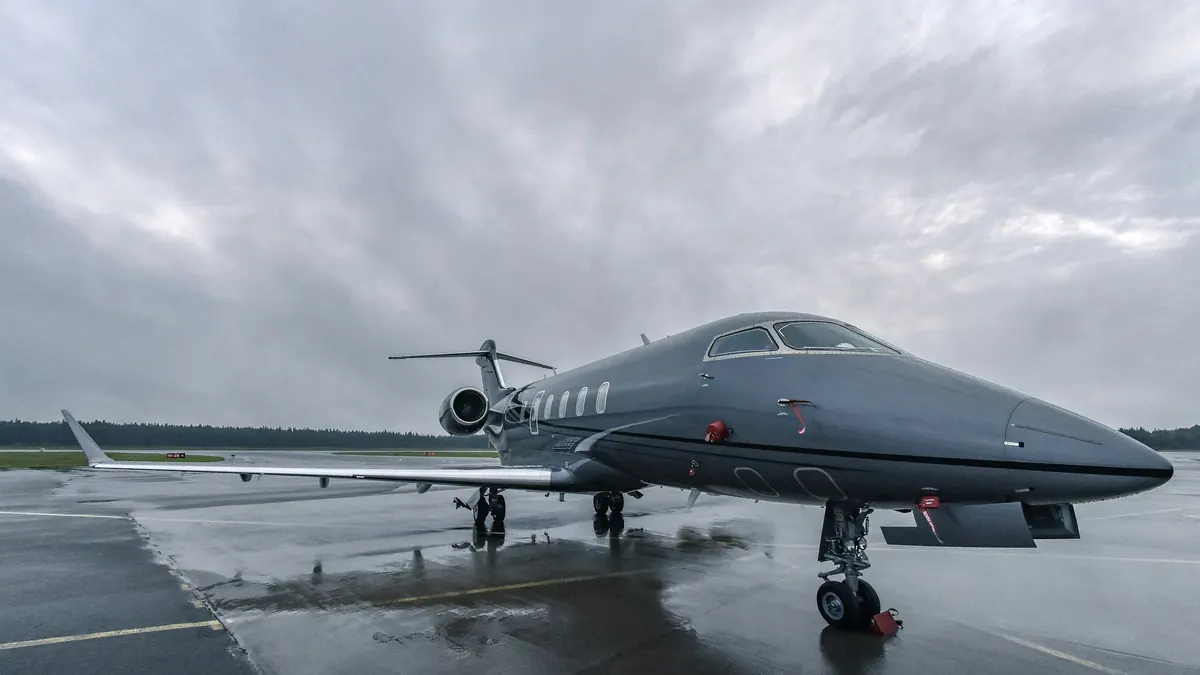 A dark business jet on a wet ramp under heavy cloud